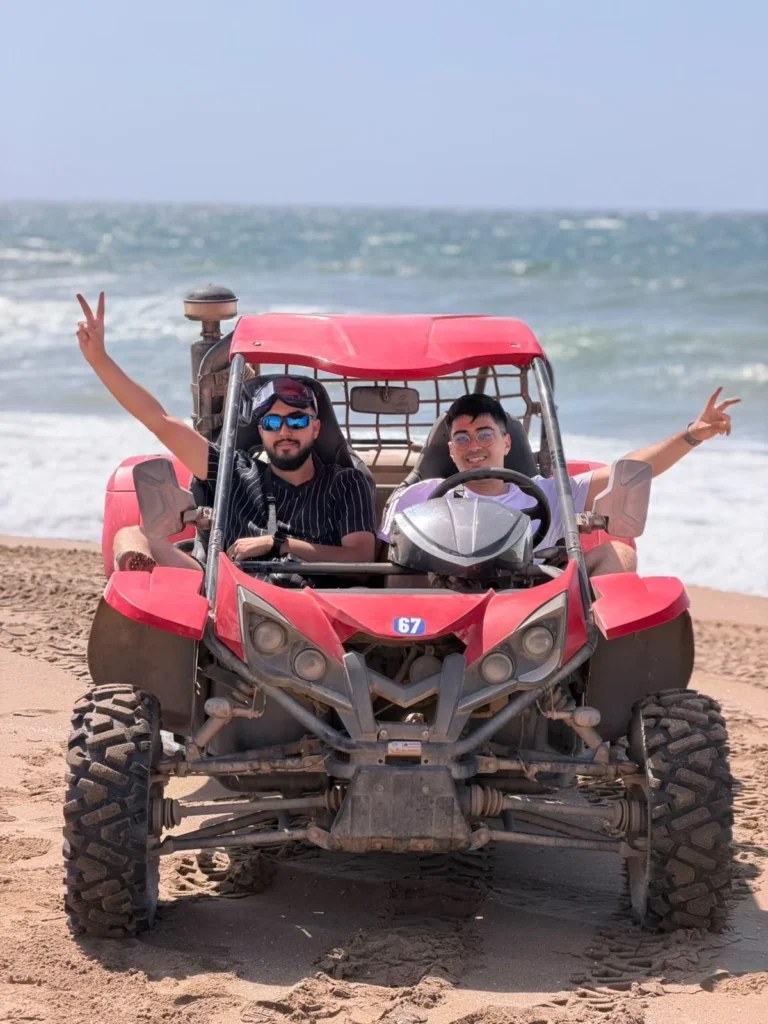 Two riders in a red off-road buggy on the sand near the sea