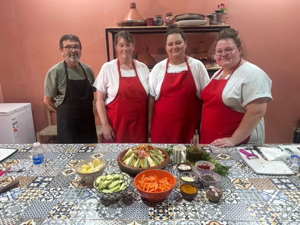 Four people in aprons standing behind a table of prepared vegetables and spices