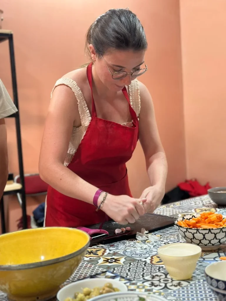 Guest in a red apron cutting carrots at a cooking class table