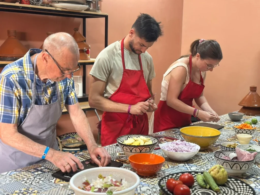 Three guests in aprons chopping vegetables at a patterned tile cooking table