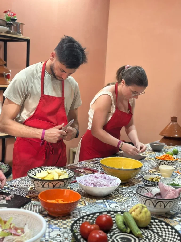 Two guests in red aprons preparing vegetables beside bowls of ingredients