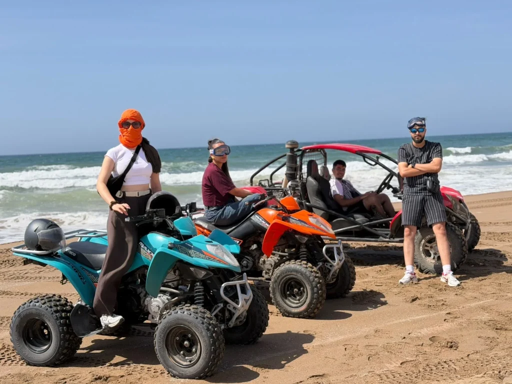 Two quad bikes and a buggy parked on the sand with visitors and waves behind