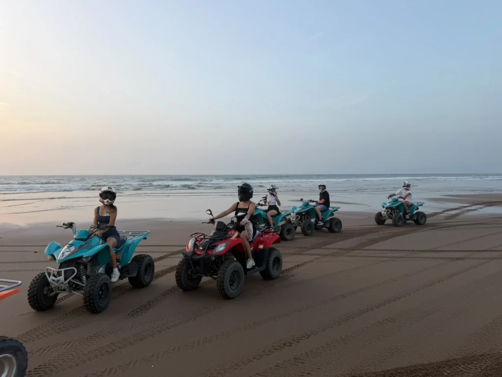 Group of riders on quad bikes driving along a wide sandy beach