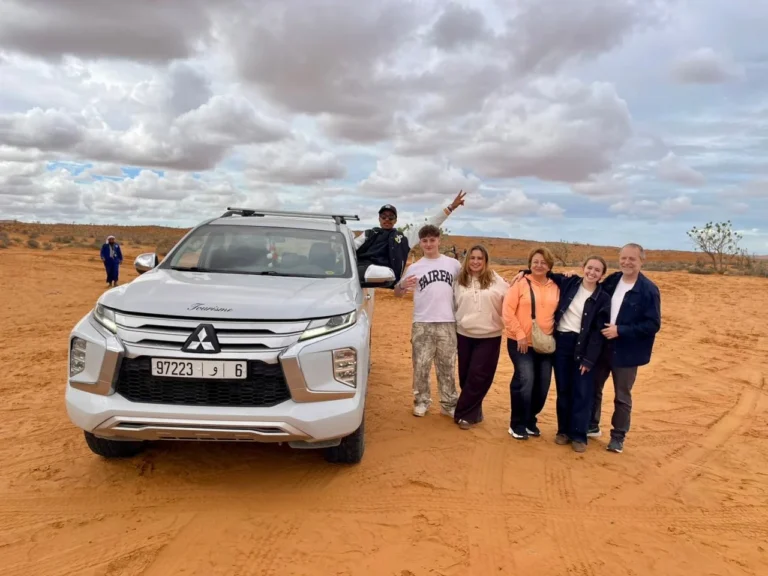 White 4x4 jeep parked on orange sand with a group of visitors standing beside it